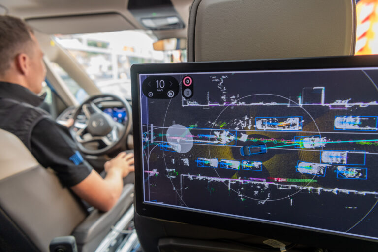 Blick vom Rücksitz des autonomen Shuttles EDGAR auf den Bildschirm, der technische und grafische Daten Umgebungsdaten anzeigt.