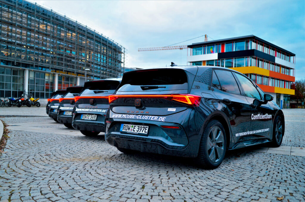 Rückansicht von fünf schwarzen Elektroautos der Marke Cupra, die zur Autoflotte des ComfficientShare-Projekts gehören. Im Hintergrund sind Gebäude des Campus Garching zu sehen.