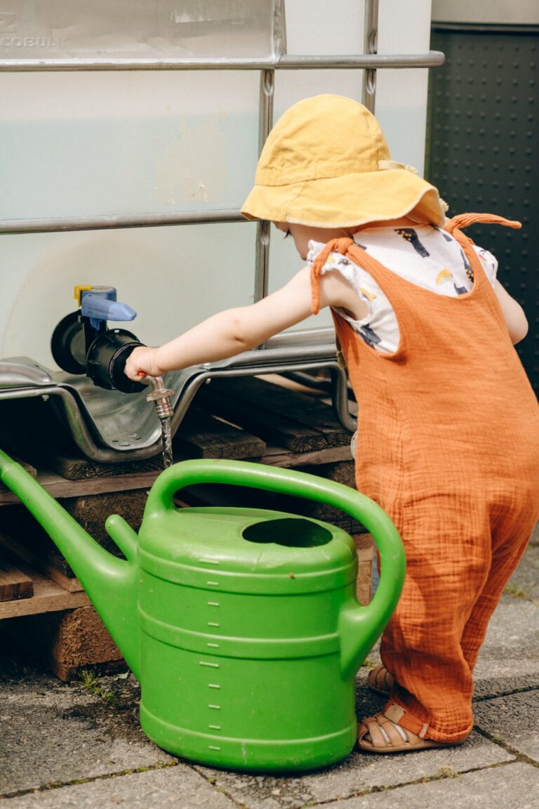 Ein Kleinkind versucht, eine grüne Gießkanne mit Wasser aus einem Wassertank zu befüllen.
