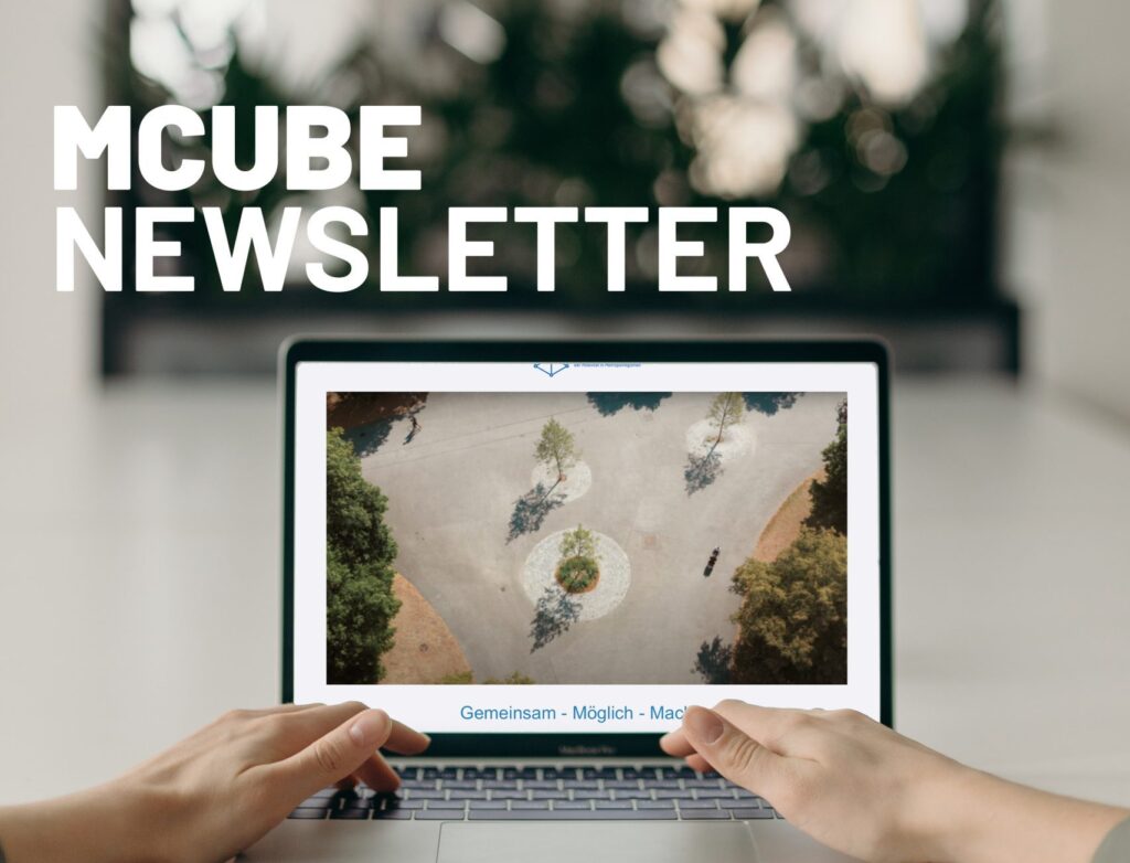 Das Bild zeigt eine Person, die auf einem Laptop tippt. Auf dem Bildschirm ist eine Luftaufnahme eines Platzes mit Bäumen und Gehwegen zu sehen. Im Hintergrund sind Pflanzen unscharf erkennbar. Oben links auf dem Bild steht in großen weißen Buchstaben "MCUBE NEWSLETTER".