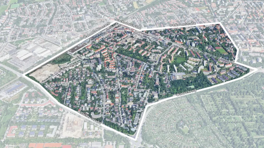 Luftbild einer städtischen Wohngegend in München, die von einer weißen Linie umrissen ist. Die Grenzen des Gebiets verlaufen entlang der Straßen „Bahnhof Moosach“, „Dachauerstraße“, „Pelkovenstraße“, „Wintrichring“ und „Allacher Straße“. Innerhalb des Bereichs sind verschiedene Wohngebäude, Grünflächen und Straßen zu erkennen.