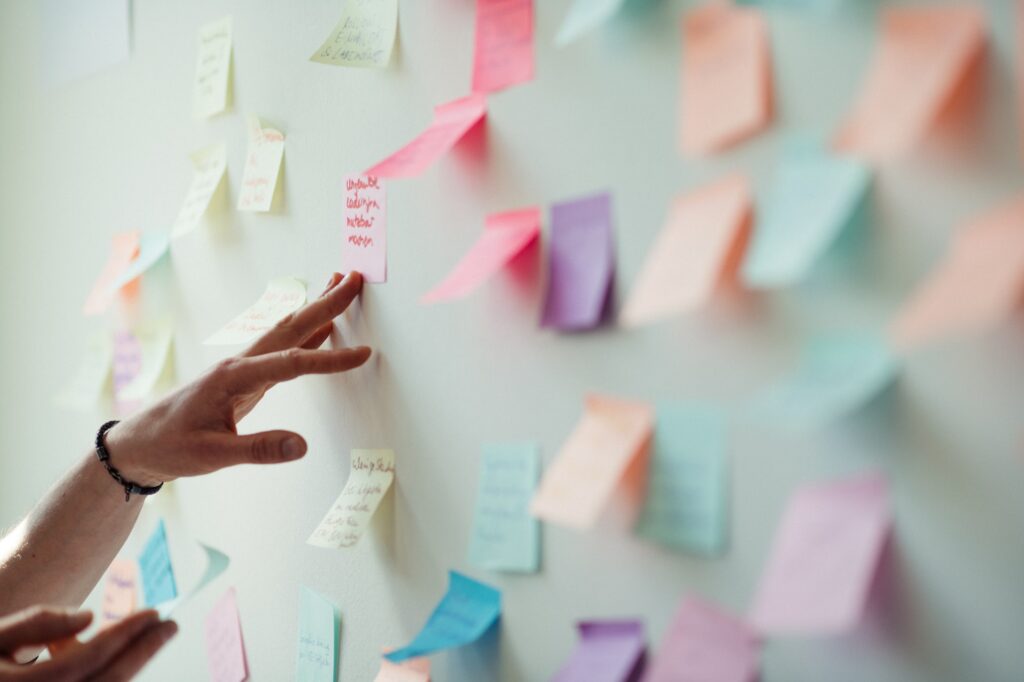 Titelbild für unseren Bereich "Themen", welches beschriftete Postits in verschiedenen Farben auf einem Whiteboard zeigt. Ein Posit wird von einer Hand glattgestrichen und genauer angeschaut.