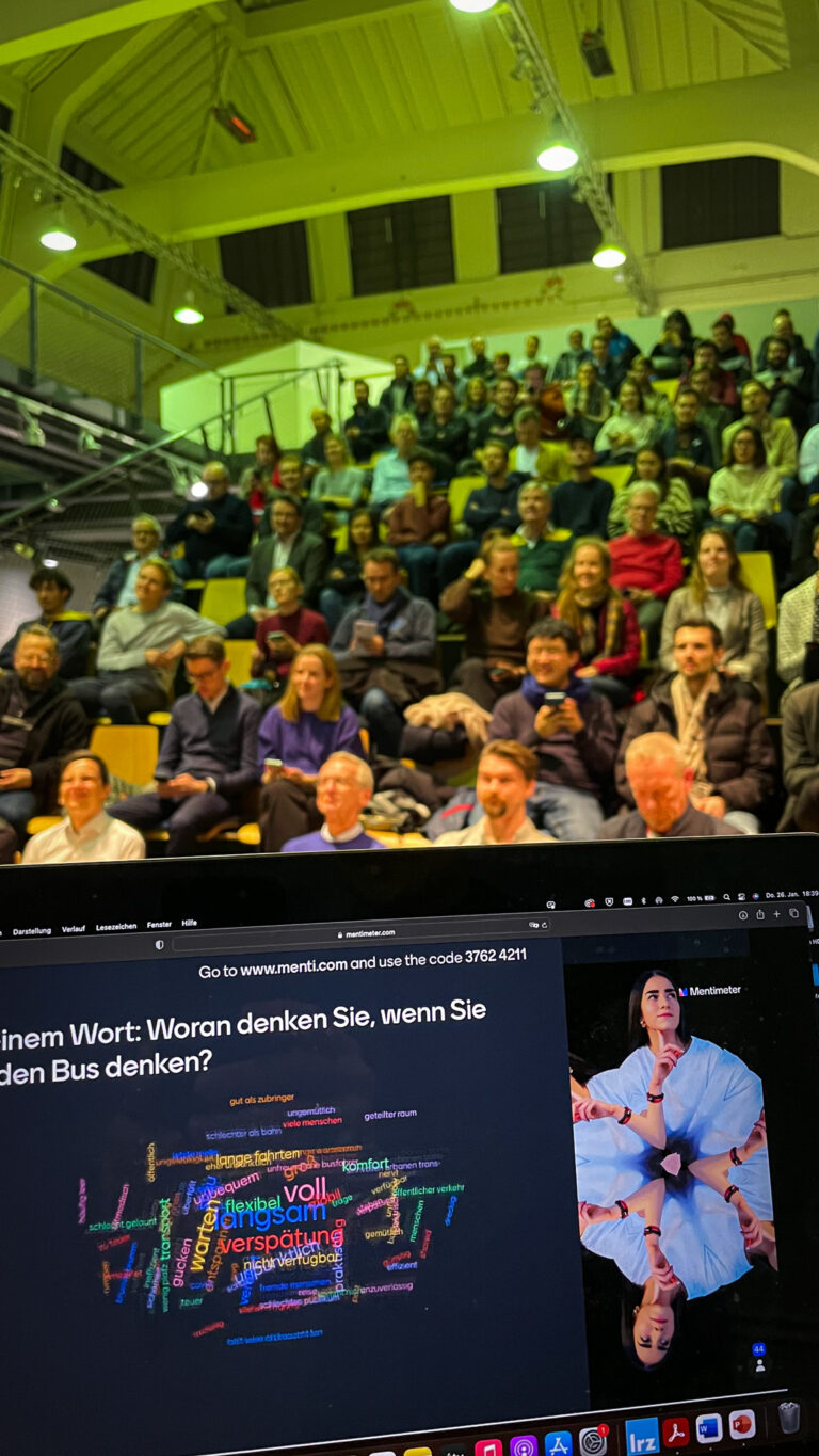 Blick von der Bühne, über den Laptop des Moderators, auf das Publikum im Verkehrszentrum des Deutschen Musuems (Halle 3) der Speaker Series #7 mit dem Thema "Das System Bus radikal neu gedacht".