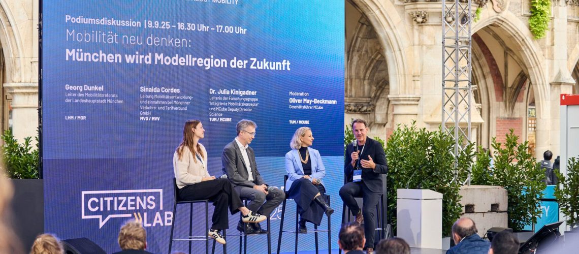 Blick auf die Bühne des Citizens Lab, auf der vier Personen (zwei Frauen und zwei Männer) eine Diskussion über das Thema "Mobilität neu denken: München wird Modellregion der Zukunft" führen.